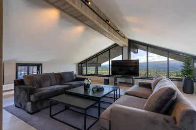a living room with couches and a tv and large windows at Stølstunets toppetasje in Beitostøl
