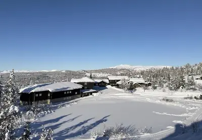 a building covered in snow next to a pond at Nydelig utsikt, ski in out, 3 soverom in Aurdal