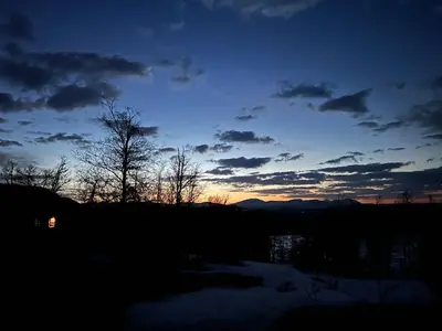 a sunset over a field with trees and a body of water at Bjørkebo in Ål - cabin in hiking and skiing area in Ål
