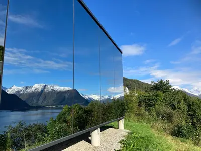 a glass building with a view of a lake and mountains at Glimre Romsdal - Eksklusivt speilhus ved Åndalsnes in Isfjorden