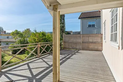a deck with a wooden railing and a blue house at Sentral og koselig leilighet! in Lillehammer