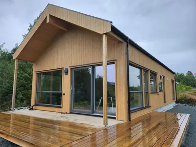 a small house with glass windows on a wooden deck at Nyoppført hytte med mulighet til å leie badestamp in Levanger
