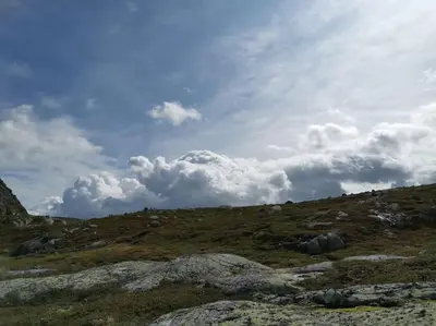 a grassy hill with rocks and a cloudy sky at Høyfjellshytte in Flå