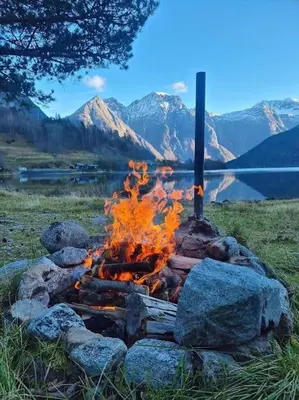 a fire pit with rocks and a lake and mountains at Jovollstua i Eresfjord med båt til leie in Øverås