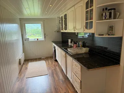 a kitchen with white cabinets and a wooden floor at Hus i Syvde in Sylte