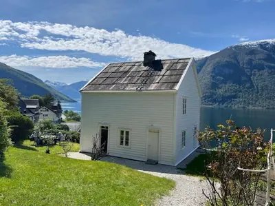 a white house on a hill next to a body of water at Nyrestaurert hus fra 1700-tallet in Bjørgo