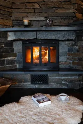 a stone fireplace with a book on a furry floor at Tovebu Superior 9-sengshytte in Geilo