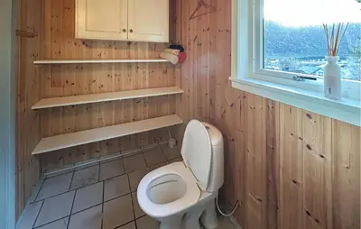 a bathroom with a toilet with wooden walls and a window at Cozy Home In Nerlandsøya Grunnkrets in Kvalsvik