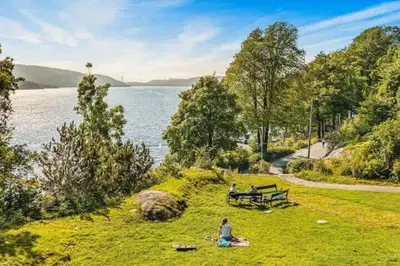 a group of people sitting on the grass near the water at Dinbnb Apartments l Free Parking l 5 Min From Torget l Nearby Coast I Newly Furnished in Bergen