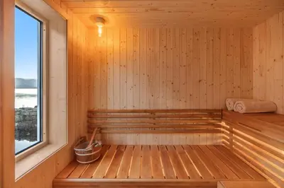 a wooden sauna with a window and a bucket at Exclusive fjord getaway with sauna in Leirgulen