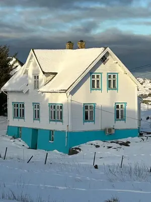 a white house with blue trim in the snow at Øyperlen in Hernar