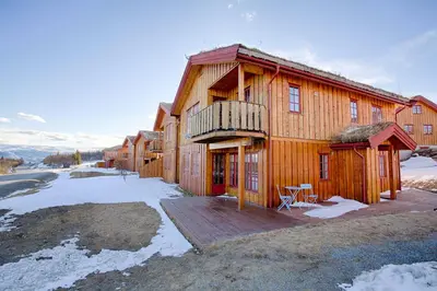 a large wooden house with a deck in the snow at Perfectly Located With Ski Access And Sauna in Beitostøl