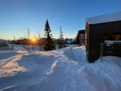 a house in the snow with the sun setting behind it at Stylish Mountain Cabin In Hallingdalen in Flå