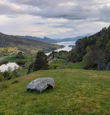 a rock in the grass on a hill with a lake at Vassel gård in Herand