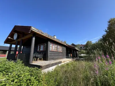 a wooden house with a porch and a field at Nostalgic Cabin With 3 Br, Fireplace, And Terrace in Beitostøl