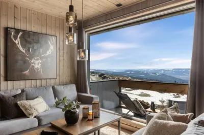 a living room with a couch and a table and a large window at New modern apartment with ski in out in Hafjell in Hafjell
