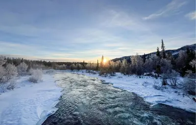a river covered in snow with the sun in the background at Moderne Hytte Midt I Skibakken in Ryfoss