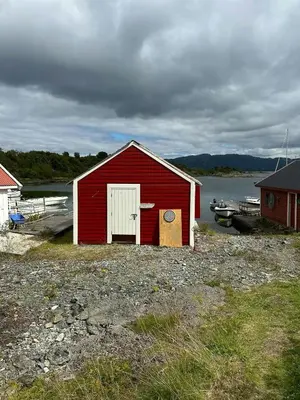 a red building with a white door and a boat at Idyllic Cabin At Bømlafjorden With Sea View in Mosterhamn