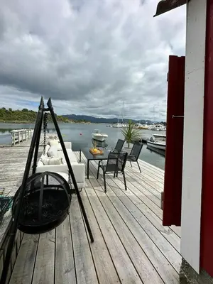 a wooden deck with a gondola and chairs on a dock at Idyllic Cabin At Bømlafjorden With Sea View in Mosterhamn