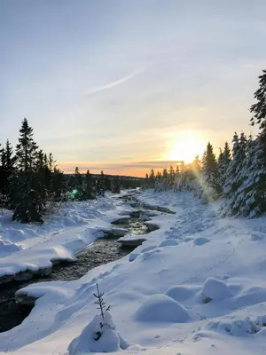 a river covered in snow with the sun setting in the background at Modern Mountain Cabin With Panoramic Views in Sjusjøen