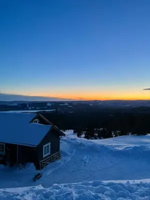 a house in the snow with the sunset in the background at Modern Mountain Cabin With Panoramic Views in Sjusjøen