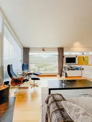 a living room with a large window and a kitchen at Charming Cabin Overlooking Vegglifjell in Kravikfjord