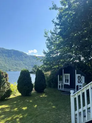 a small blue house with a white fence and a lake at Cabin With Shoreline By Brusdalsvannet Lake in Ålesund