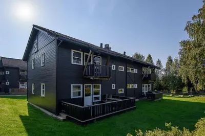 a large black house with a green yard at Hafjell Alpinlandsby Apartment 43 in Hafjell