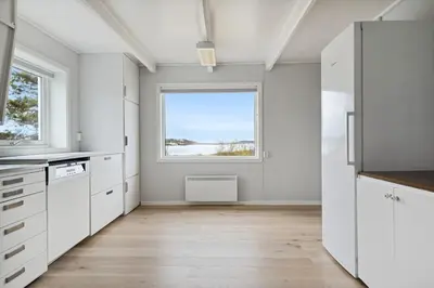a kitchen with white cabinets and a large window at Idyllisk perle ved sjøen! in Frøya