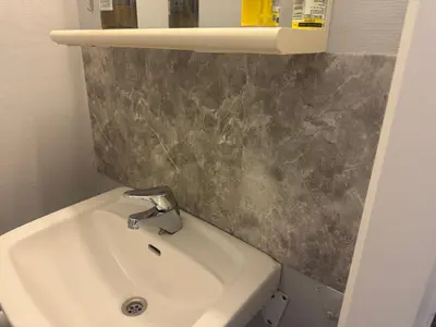 a bathroom with a white sink and a gray wall at Small apartment in Elnesvågen in Svinøya