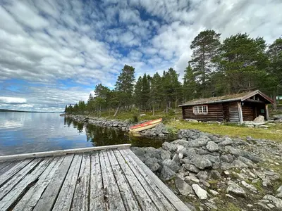 a cabin on the shore of a lake with a boat at Family cabin by the lake at Haugen, Femundsmarka in Elga