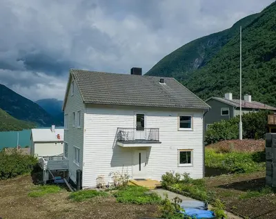 a white house with a balcony in front of mountains at Charming 2-bedroom loft by UNESCO site Jotunheimen and Vettifossen! in Årdalstangen