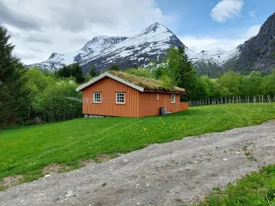 a house with a grass roof with mountains in the background at timber cabin Eresfjord med båt til leie in Øverås