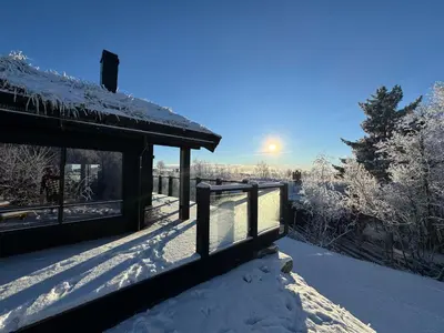 a house covered in snow with the sun in the background at New modern cabin in Beitostølen in Beitostøl