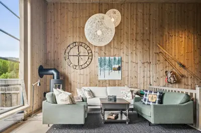 a living room with two chairs and a couch and a clock at Very central and fresh apartment 4 bedr, 10p 2 floors, sauna, ski in and out in Trysil