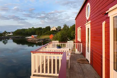 a red house with a deck next to a body of water at Eget hus i sjøkanten ved fjorden in Langevåg