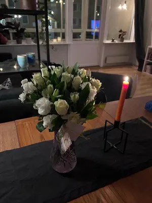 a vase of white flowers on a table with a candle at 2 bed apartment in Trondheim