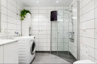 a white bathroom with a washing machine and a shower at Fin leilighet for Ski VM in Trondheim