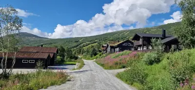 a dirt road in front of houses and mountains at Panorama Cabin - Stunning Mountain Views and Outdoor Jacuzzi Option in Bjorli