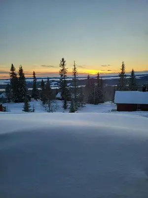a field covered in snow with a barn and trees at Sunny Cabin With Panoramic Views At Sjusjøen in Sjusjøen