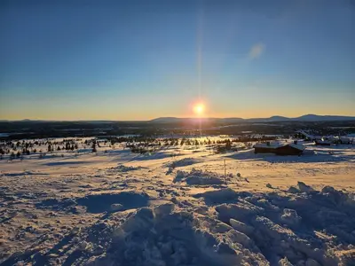 a snowy field with the sun setting in the background at Varden in Sør-Fron