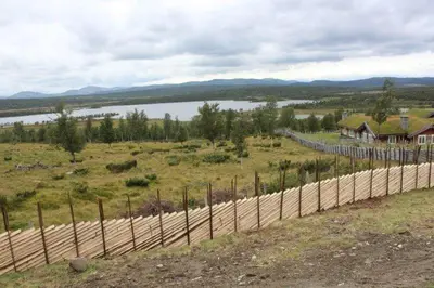 a fence in a field with a house and a lake at Hytteperle Gålå, Vakre Lauvåsen, Hønhuset in Sør-Fron