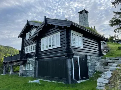 a black house with a chimney on a hill at Cozy cabin apartment, ski-in ski-out at Kvitfjell in Kvitfjell