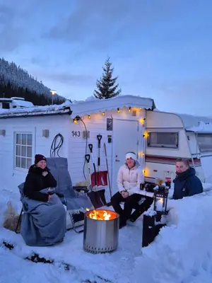 three people sitting in the snow in front of a camper at Trysil Campingvogn Ski in-out in Trysil
