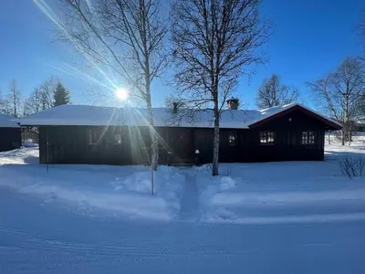 a house in the snow with the sun shining on it at Charming Mountain Retreat Near Ski Trails And Beitostølen Center in Beitostøl