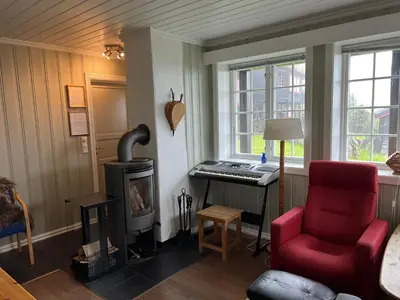 a living room with a piano and a red chair at Skiidyll Med Utsikt Og Peis in Beitostøl