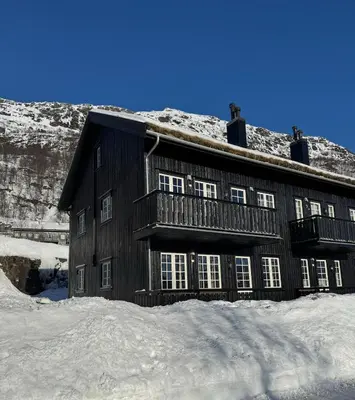 a wooden building in the snow with a mountain at Apartment Røldal in Håra