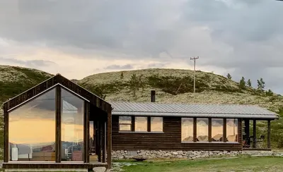 a wooden house with large windows in front of a hill at Architect Drawn Holiday Home Near Rondane Park in Høvringen