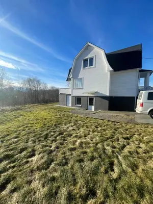 a white house on a hill with a grass field at Sokkelleilighet i enebolig i Ålesund nær stranden in Ålesund
