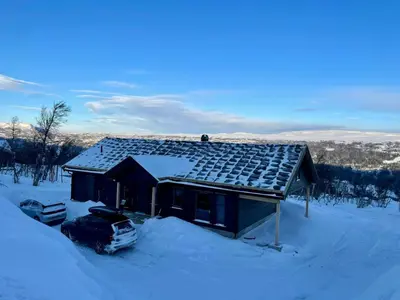a house covered in snow with a car parked in front at Mountain Cabin At Hardangervidda in Uvdal